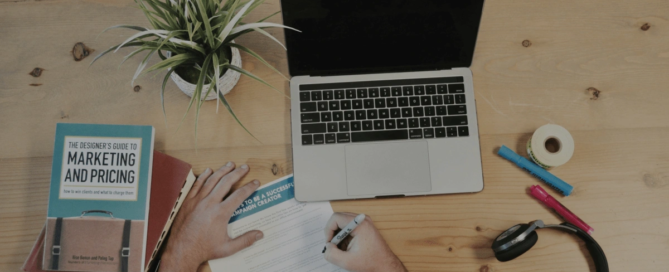 View of person's hands and a couple of books on table with computer that is turned off