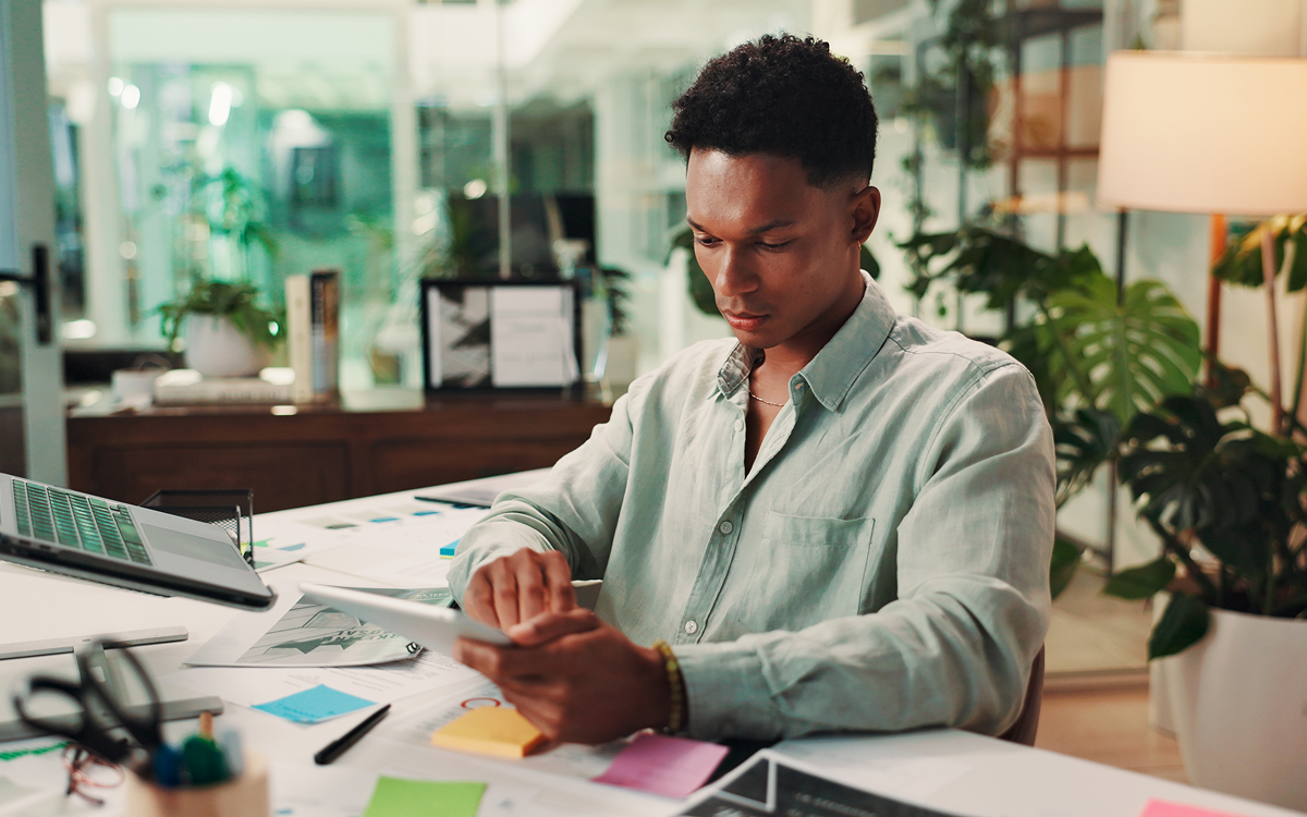 Person reviewing documents and notes at a desk in a modern office workspace with plants and natural light.